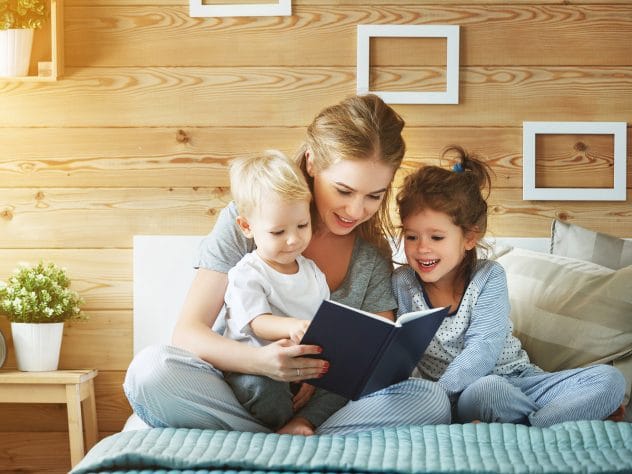 Mother reading a book to her two young children in cozy wooden room