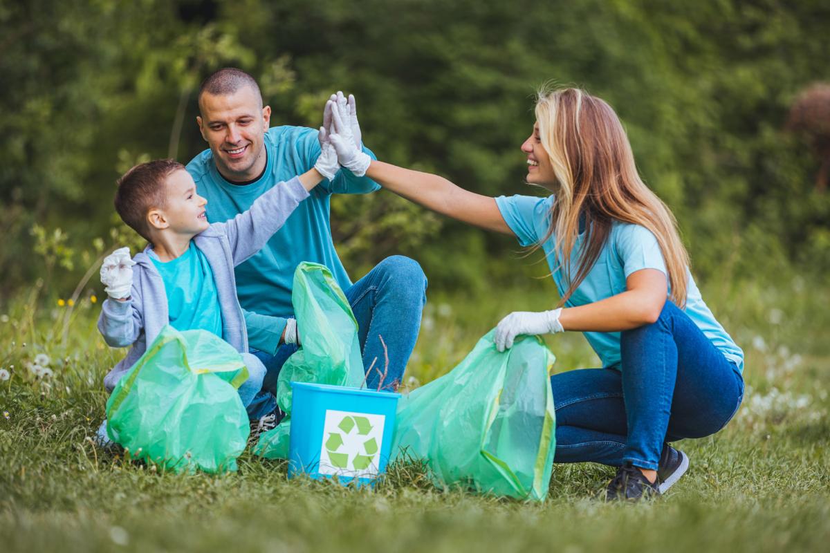 Family cleaning up park together recycling with green bags