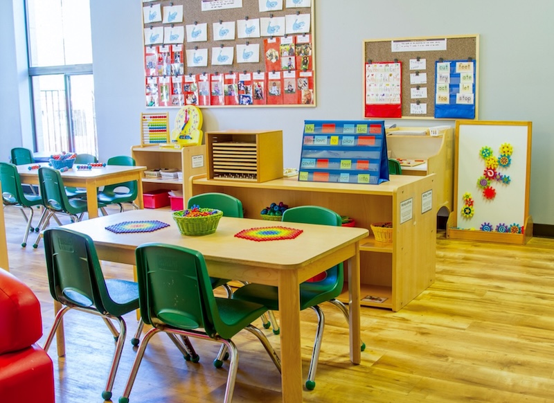 Bright classroom with colorful educational materials and small wooden tables and green chairs