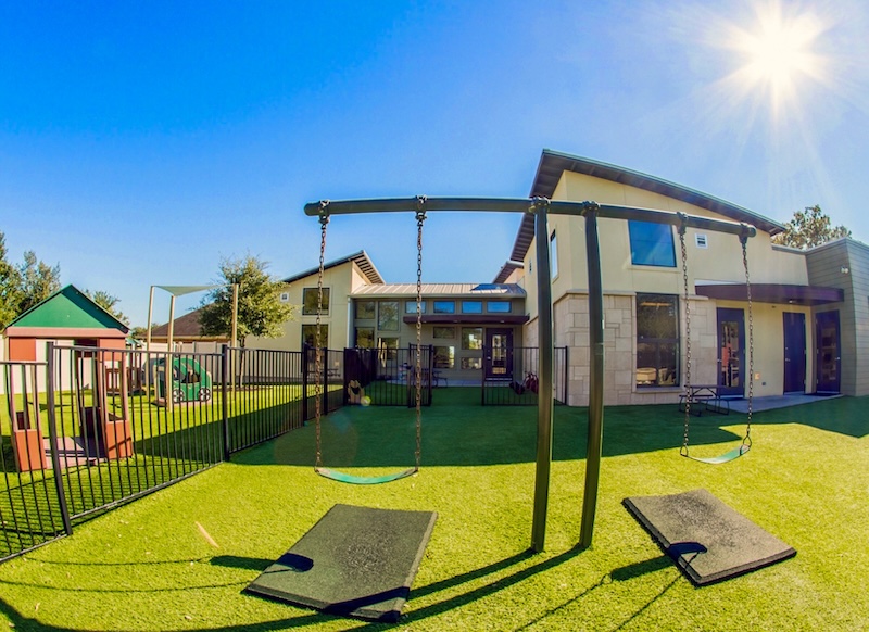 Sunny daycare playground with swings and artificial grass near a modern building