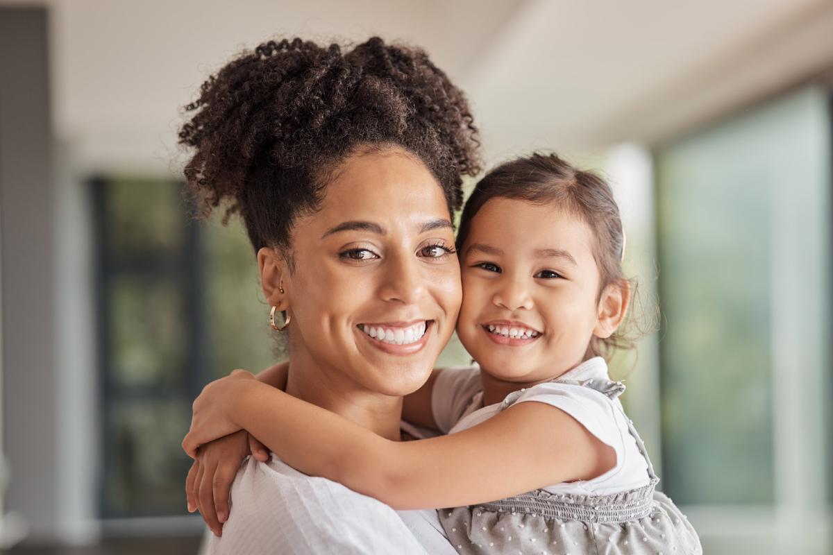 Smiling mother and daughter hugging indoors with natural light