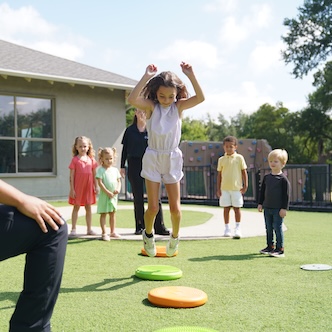 Children playing a jumping game on a sunny day in a grassy backyard