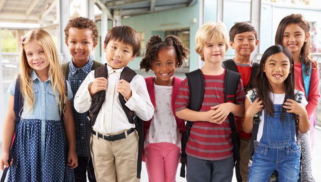 Smiling group of diverse children with backpacks standing in a school corridor