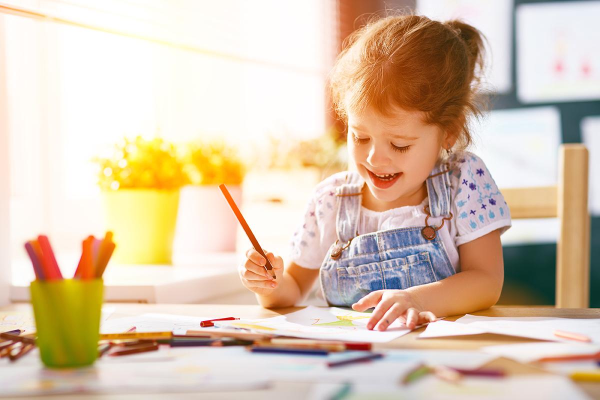 Young girl drawing with colored pencils at a sunlit table