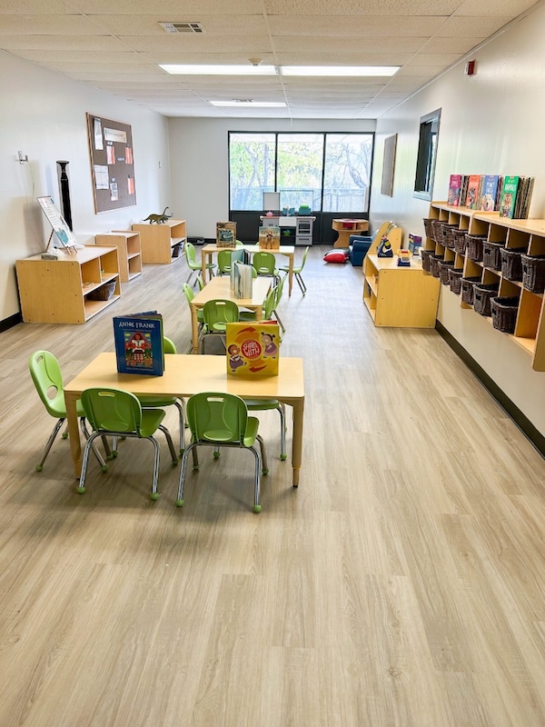 Bright preschool classroom with green chairs wooden shelves books and educational toys