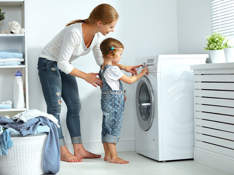Mother and daughter using a washing machine in a laundry room