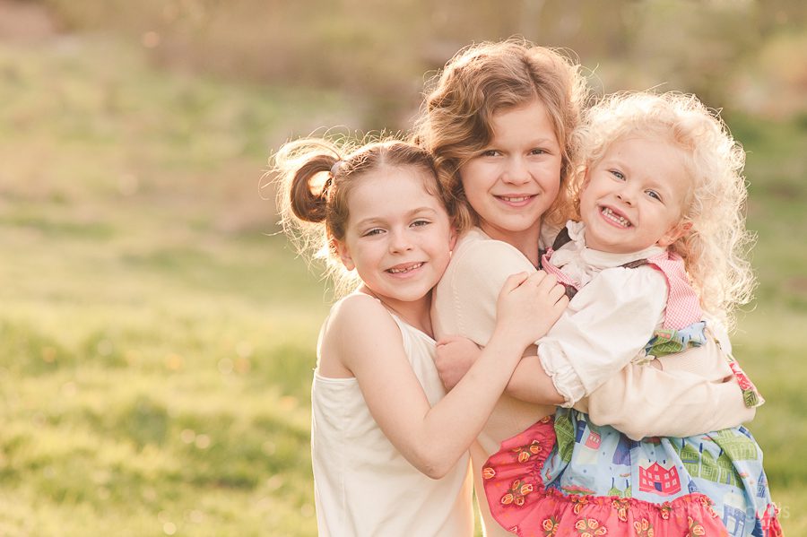 Three smiling children embracing in a sunny field