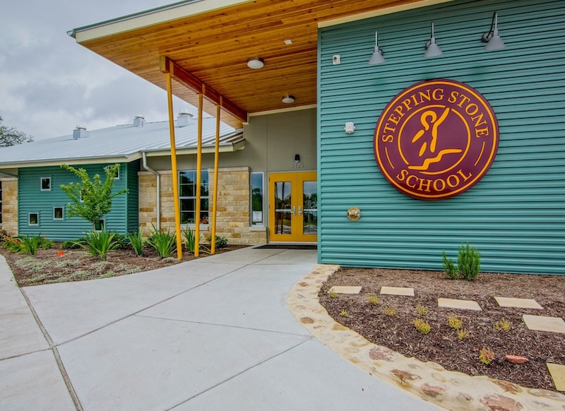 Modern school building entrance with green siding and circular logo sign.