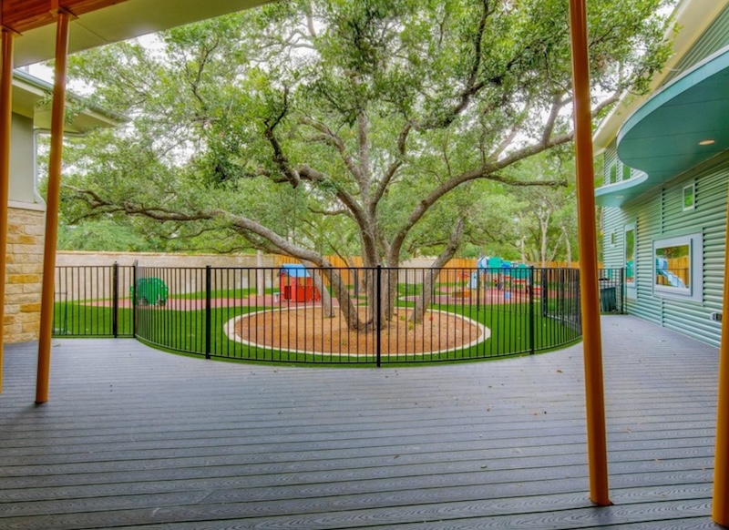 Outdoor playground with large tree and fenced area on a wooden deck background