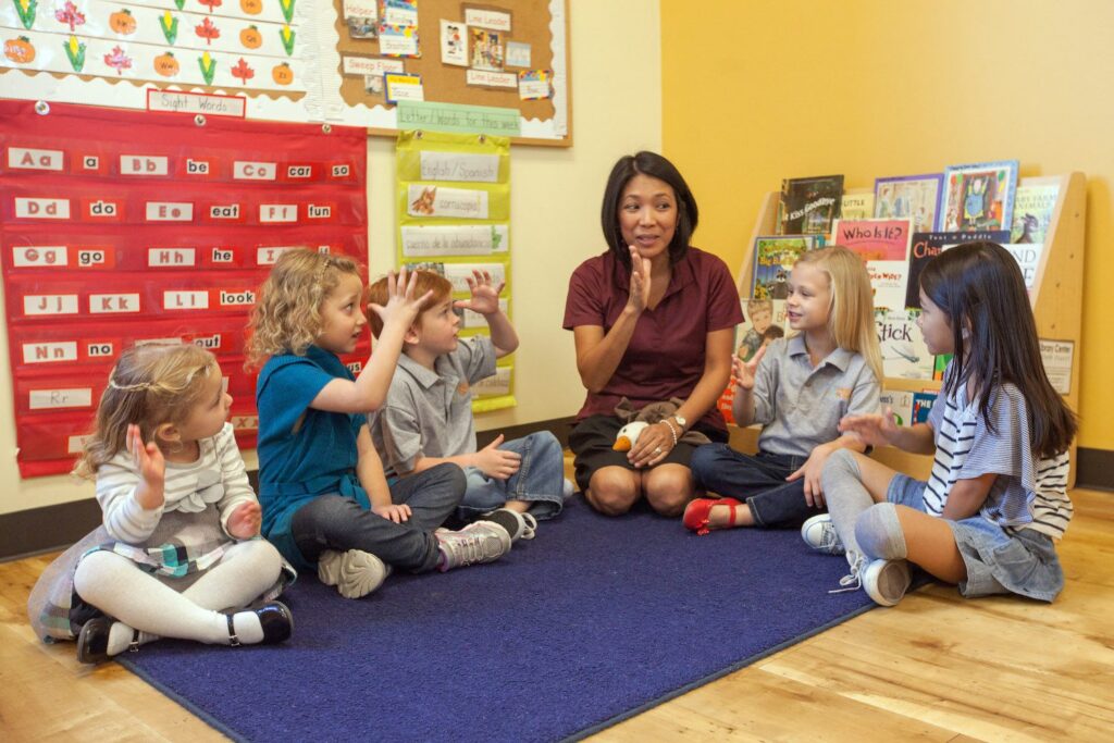 Teacher engaging with young children during a classroom activity on a colorful rug.