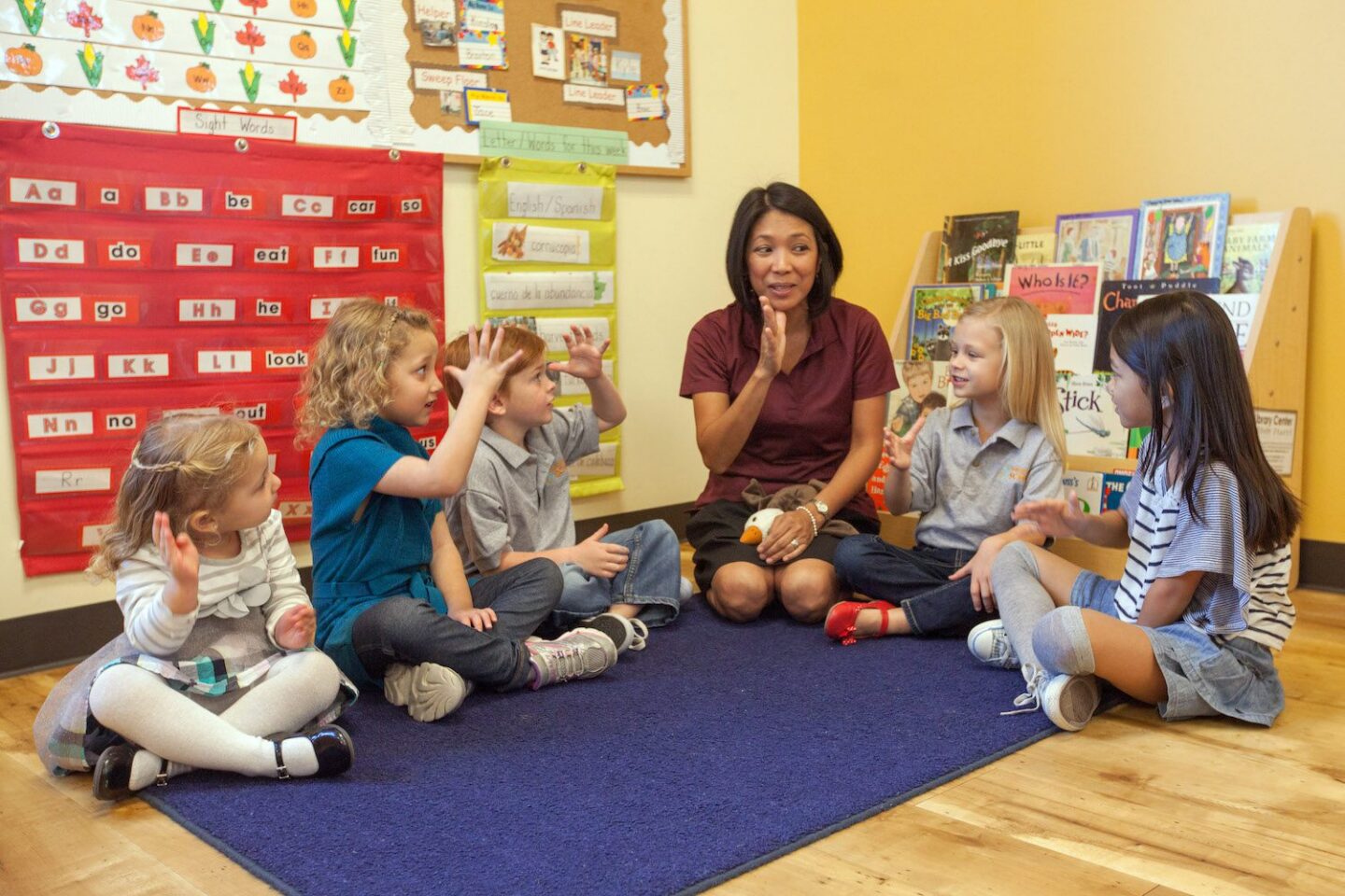 Teacher engaging with young children during a classroom activity on a colorful rug.