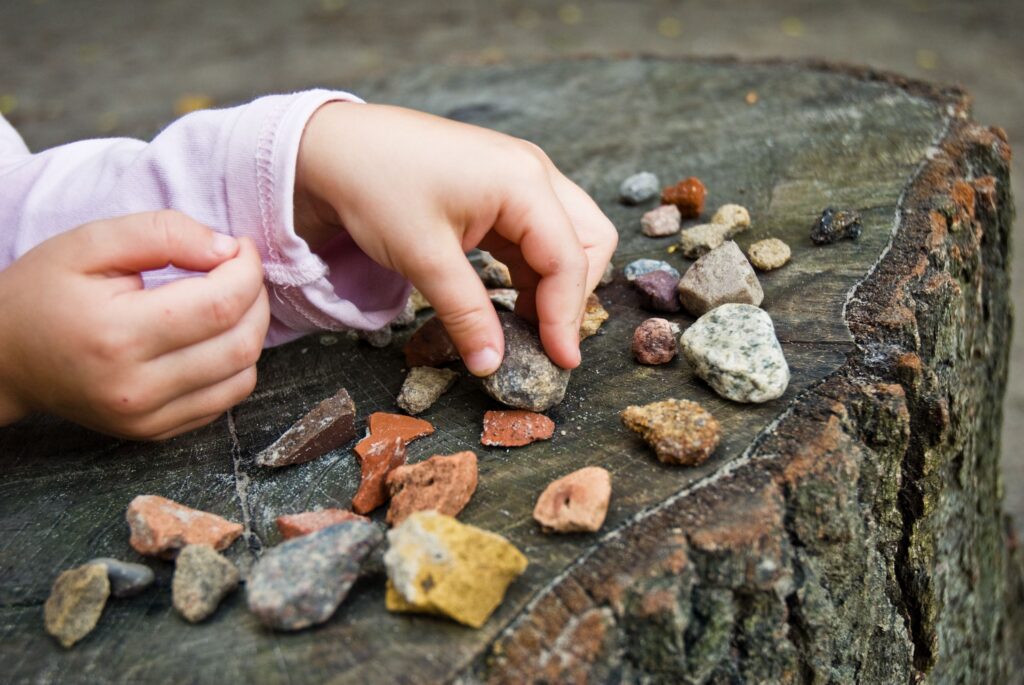 Child playing with colorful rocks on a tree stump