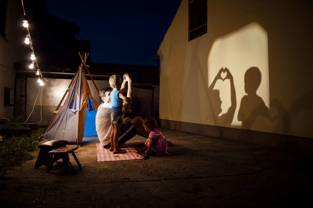 Family creating shadow puppets on a wall at night in a backyard camping scene