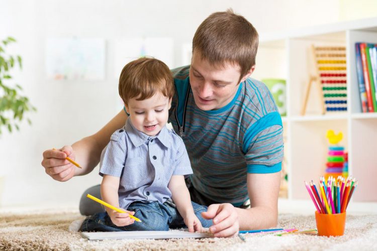Father and son drawing together on the floor in a bright room