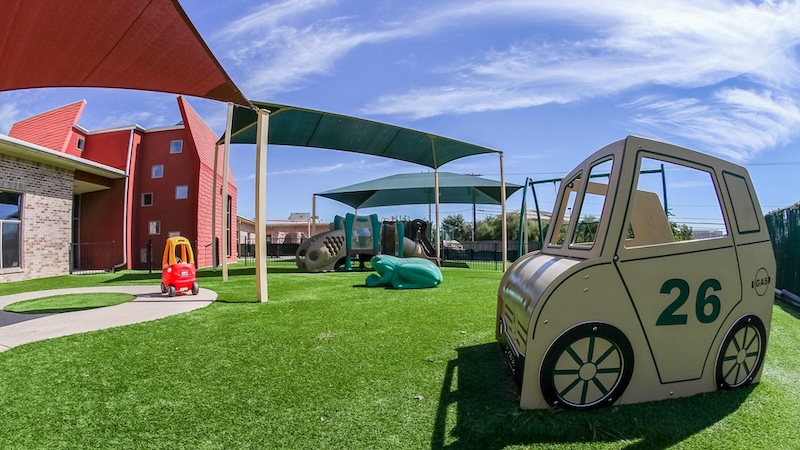 Colorful playground with toy cars and slides on artificial grass under a blue sky