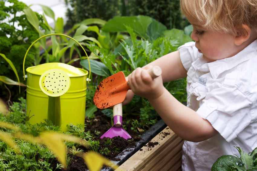 Child gardening with small spade near green watering can and plants