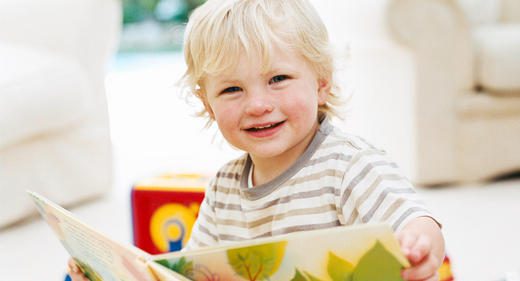 Smiling toddler with a book playing indoors on a bright day