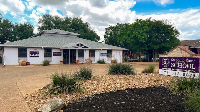 Exterior view of Stepping Stone School building surrounded by plants and trees under a partly cloudy sky.