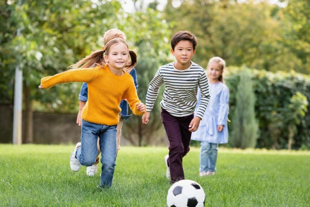 Children playing soccer on a grassy field in a park on a sunny day