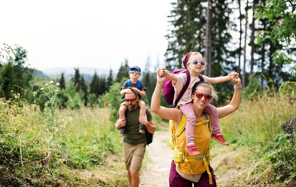 Family hiking on a forest trail with kids on shoulders on a sunny day