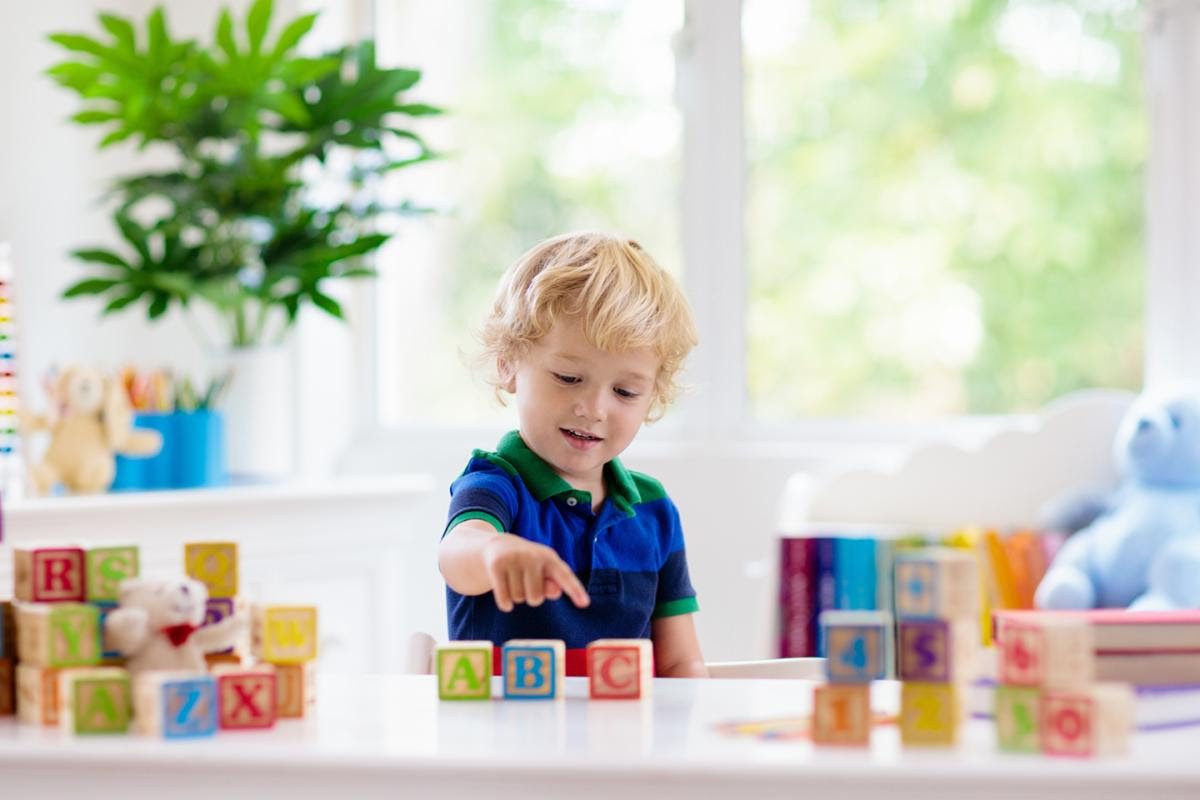 Child playing with alphabet blocks at a table in a bright room